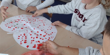 Powiększ grafikę: Dzieci malują palcami wycięte z papieru jabłko.
