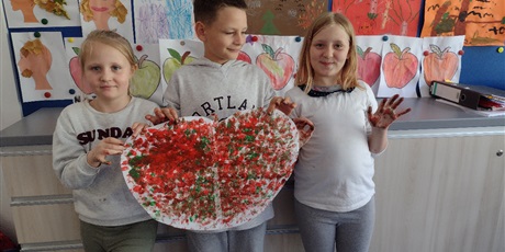 Powiększ grafikę: Troje dzieci prezentuje pokolorowane palcami jabłko z papieru.