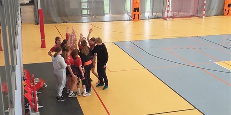 Powiększ grafikę: Stojąca grupka dziewczynek razem z trenerką na turnieju piłki ręcznej.