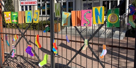 Powiększ grafikę: Na szkolnej bramie napis -witaj wiosno i rozwiaszone kolorowe skarpetki.
