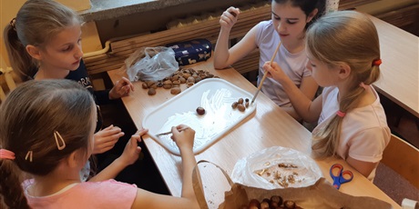 Powiększ grafikę: Dziewczynki przyklejają łupinki orzecha włoskiego i żołędzie na plastikowej tacy.