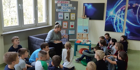 Powiększ grafikę: Uczniowie siedzą na pufach i słuchają pani Joli, jak opowiada o walorach czytania głośnego.