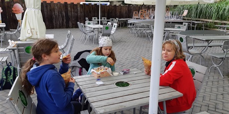 Powiększ grafikę: Trzy dziewczynki siedzą przy stole na świeżym powietrzu i jedzą frytki.